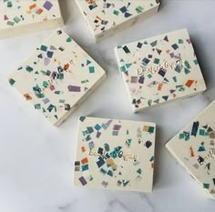 six white marble coasters with colorful confetti designs on the top and bottom