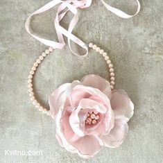 a pink flower and pearl necklace on a gray background