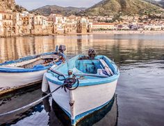 two small boats tied to the dock in front of some buildings and water with mountains in the background