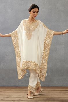 Ivory kaftan with placement vintage pattern, cut work lace hem details, contrast gold dori, sequin, adda hand embroidered yoke and borders. Paired with pants with embroidered border.
Components: 2
Pattern: Hand Embroidered
Type Of Work: Dori, Sequin, Lace and Adda Work
Neckline: V Neck
Sleeve Type: Flared Sleeves
Fabric: Silk Crepe, Cotton Voile
Color: Ivory
Other Details: 
Cut work lace hem
Printed inner border
Occasion: Destination Wedding,Sangeet - Aza Fashions Kaftan Pattern Kurti, Embroidery Kaftan, Designer Kaftan, Kaftan Set, Dori Embroidery, Kaftan Pattern, Embroidered Kaftan, Dangler Earrings, Pant Set For Women