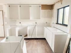 an empty kitchen with white cabinets and wood flooring in the process of remodeling