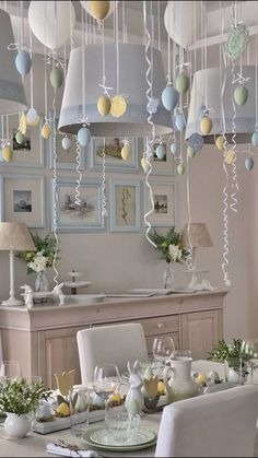 a dining room table is set with white chairs and balloons hanging from the ceiling above it