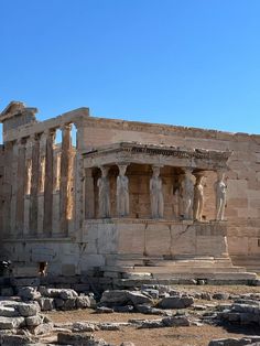 an ancient building with statues on the front and side walls, surrounded by large rocks