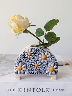 a white rose sitting in a blue and white vase on top of a book with the words, the kinfok home