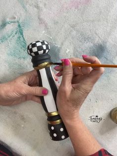 a woman is holding a pencil and painting a black and white object with gold trim