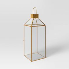 a gold metal and glass lantern with a handle on the top, in front of a white background