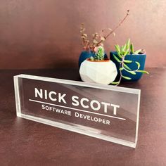 a clear acrylic sign sitting on top of a table next to a potted plant