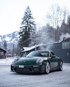 a green sports car parked in front of a building with snow on the ground and trees