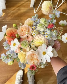 a bouquet of flowers is being held by someone's hand on the floor in front of a chair