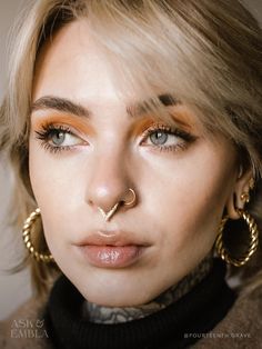 a woman with piercings on her nose wearing gold hoop earrings and a turtle neck sweater