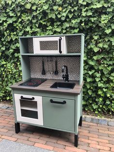 an outdoor play kitchen with sink, stove and oven in front of a green hedge