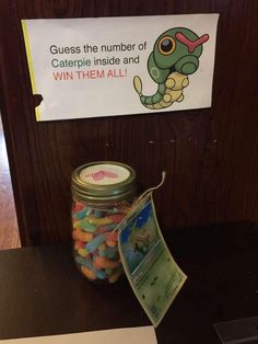 a jar filled with candy sitting on top of a table next to a sign that says guess the number of caterpi inside and win them all