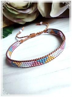 a bracelet with multi colored beads and a brown cord on top of a white table