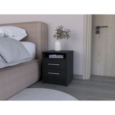 a nightstand with two drawers next to a bed and a plant in a white vase