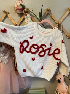 a white sweater with the word rose written on it next to other clothes and toys