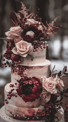 a three tiered cake with red flowers and berries on the top is surrounded by greenery