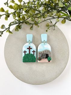 two earrings with crosses on them sitting next to a plant