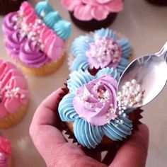 a hand holding a spoon with cupcakes decorated in pastel colors and flowers