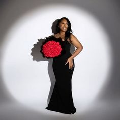 a woman in a long black dress holding a bouquet of red carnations on her shoulder