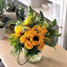 a vase filled with yellow flowers sitting on top of a wooden table next to potted plants