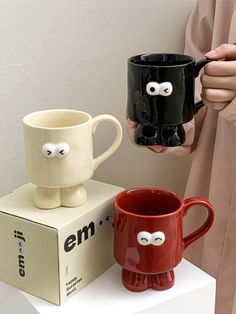 two coffee mugs with googly eyes sitting on top of each other in front of a box