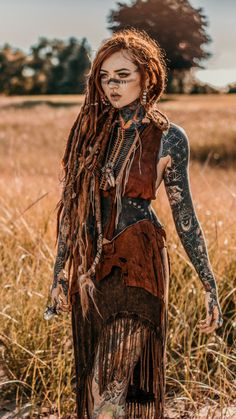 a woman with dreadlocks and tattoos standing in a field wearing a brown dress