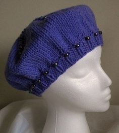 a white mannequin head wearing a purple knitted hat with black studs