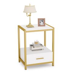 a white and gold end table with a lamp on top next to some books in front of it