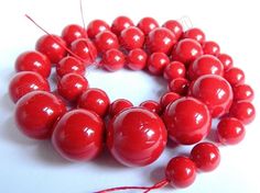 a bunch of red beads on a white surface with some string in the middle and one bead at the end