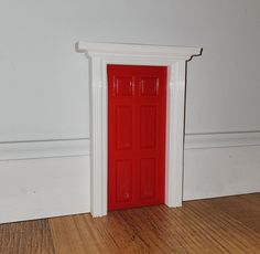 a red door is in the corner of a room with white trim and wood flooring