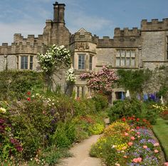 an old castle with lots of flowers in the foreground and a path leading to it