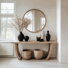 a table with vases and candles on it in front of a round mirror above two wicker baskets