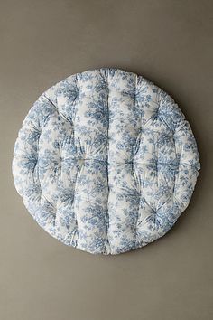 a blue and white flowered round cushion sitting on top of a gray floor next to a wall