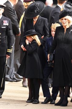 two women in black coats and hats are standing next to each other while others watch