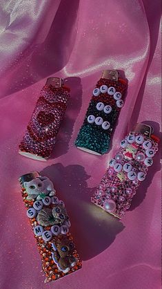 three cell phones covered in buttons and beads on a pink cloth with sequins