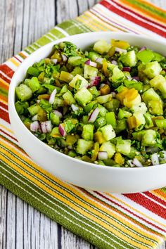 a white bowl filled with chopped vegetables on top of a striped table cloth next to a fork