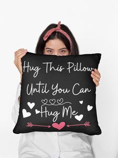 a woman holding up a pillow that says hug this pillow until you can hug me