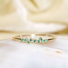 a gold ring with three green stones on the side, sitting on top of a white cloth