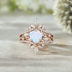 a white opal and diamond ring sitting on top of a sand covered ground next to a pine tree