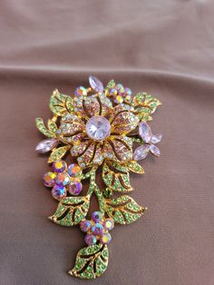 The brooch is a full floral with 1mm to 8mm pink and green crystal accents.  14k gold plated. Luxury Green Brooches For Wedding, Yellow Gold Flower Brooch Jewelry, Yellow Gold Flower Brooch, Elegant Green Jeweled Brooches, Luxury Flower Shaped Brooch Jewelry, Luxury Pink Brooch Jewelry, Gold Flower-shaped Jeweled Jewelry, Gold Party Brooches With Flower Decoration, Gold Flower-shaped Jewelry With Rhinestones