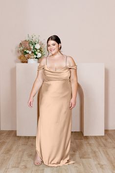 a woman in a long dress standing on a wooden floor next to a vase with flowers