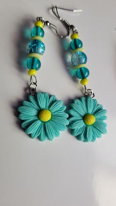 a pair of blue and yellow flowers are hanging from earrings on a white surface with beads