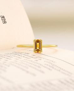 a yellow diamond ring sitting on top of an open book next to a piece of paper