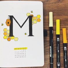 a notepad with the letter m on it next to markers and pencils,