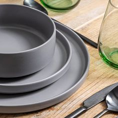 a table set with grey plates, silverware and green wine glasses on the table