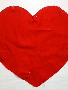 a red heart shaped piece of fabric with pins sticking out of the middle, on a white surface