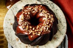 a chocolate bundt cake with nuts on top sits on a marble plate next to a red napkin