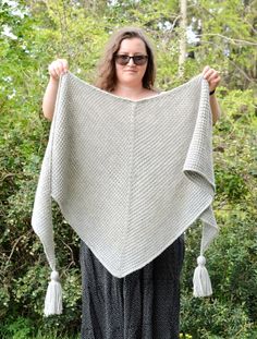 a woman holding up a shawl in front of her with trees and bushes behind her