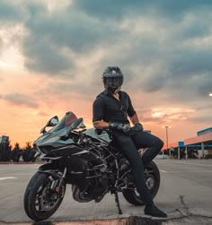 a person sitting on a motorcycle in the middle of an empty parking lot at sunset