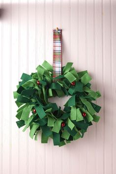 a christmas wreath made out of green paper hanging on a white wall with a checkered ribbon